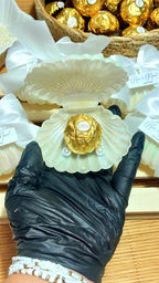 Detalle de boda con concha perlada, lazo blanco y bombón dorado personalizado con etiqueta de nombres y fecha, regalo elegante para invitados